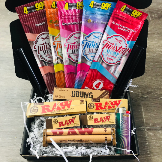 Photo of a black gift box with white shredded paper. Contents in the gift box includes five hemp wraps, rolling papers, rolling machine, joint tubes, RAW tips, and a lighter.